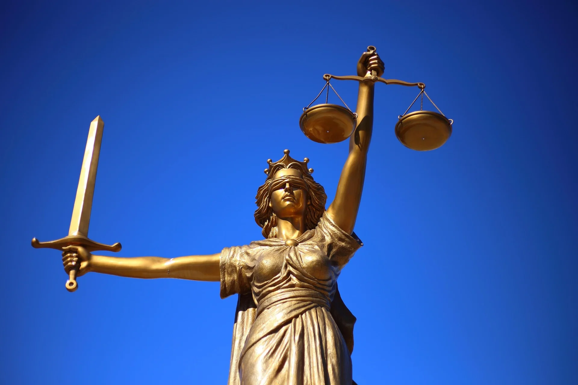 Gilded statue of Lady Justice holding scales and a sword against a clear blue sky.